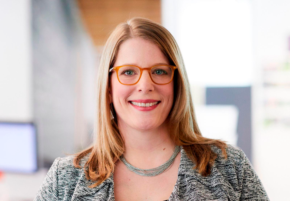 A woman wearing glasses and a necklace is smiling for the camera.