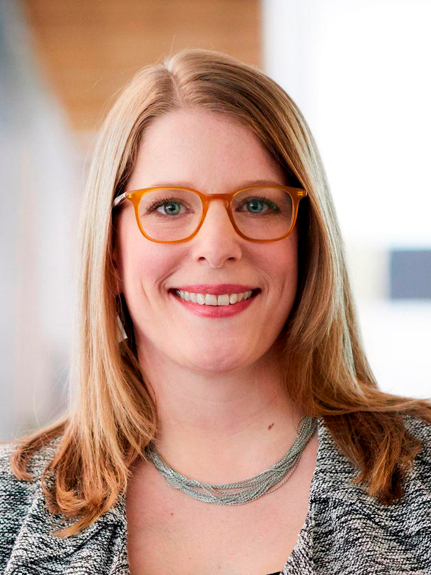 A woman wearing glasses and a necklace is smiling for the camera.