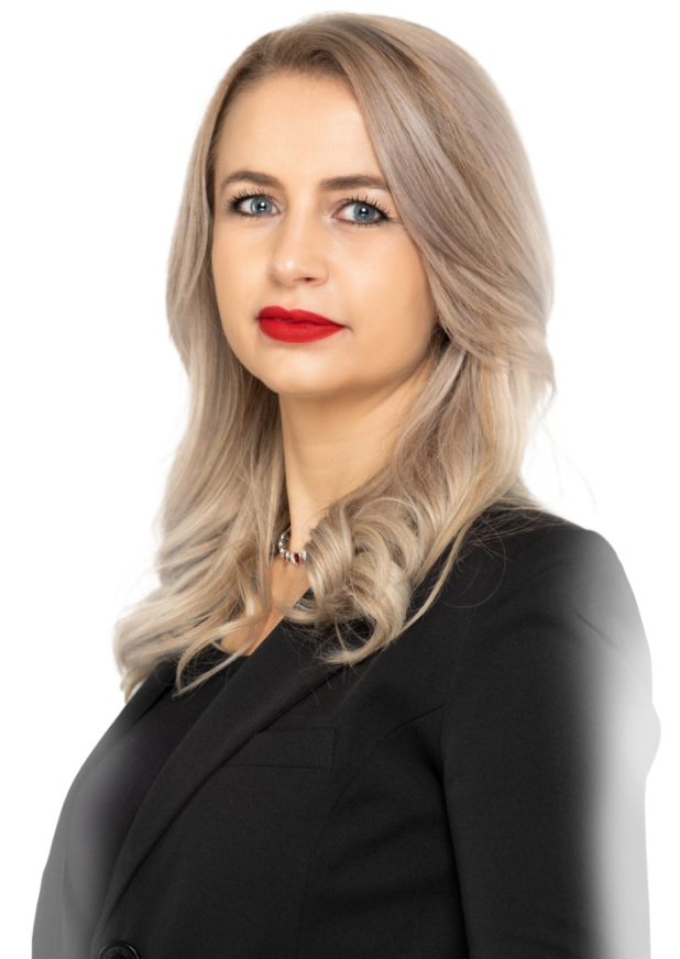 Frau mit blonden Haaren, die einen schwarzen Blazer und roten Lippenstift trägt, schaut in die Kamera.
