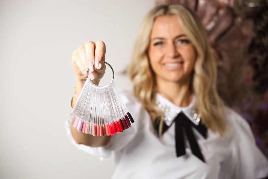 Frau hält Nagellackfarbproben in der Hand und lächelt.