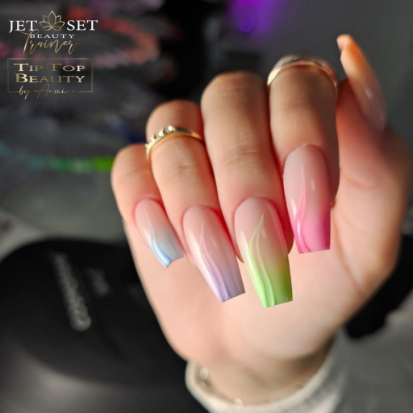 Frauenhand mit langen, sargförmigen Nägeln in Regenbogenfarben und goldenen Ringen.