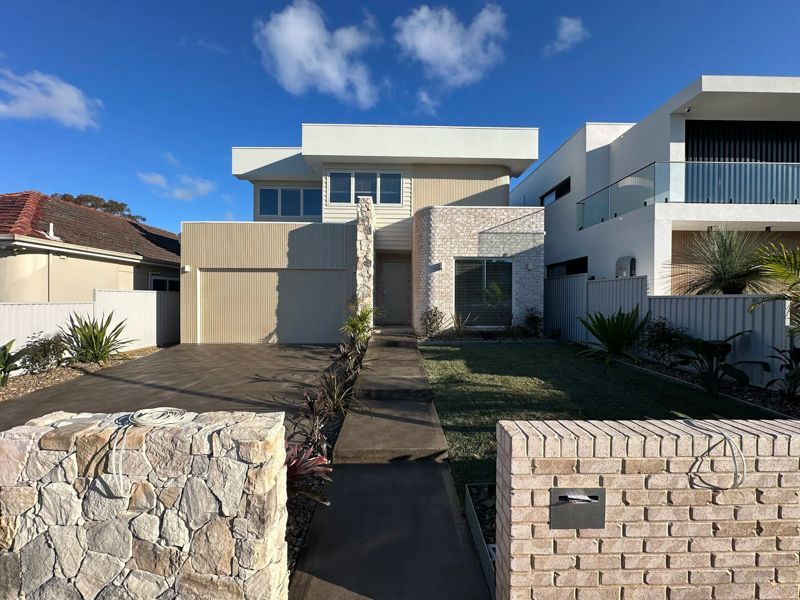 Modern house front with a narrow walkway, stone wall, and blue sky
