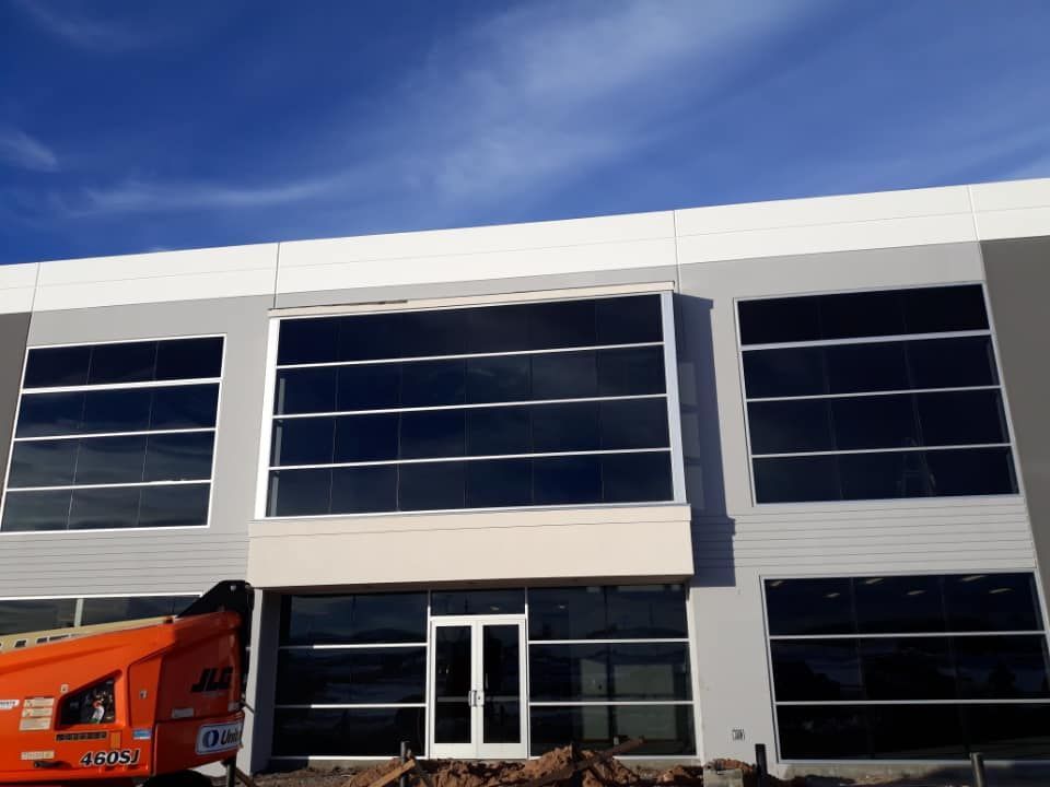 Exterior of a modern commercial building with large dark-tinted windows against a blue sky. An orange lift is visible.