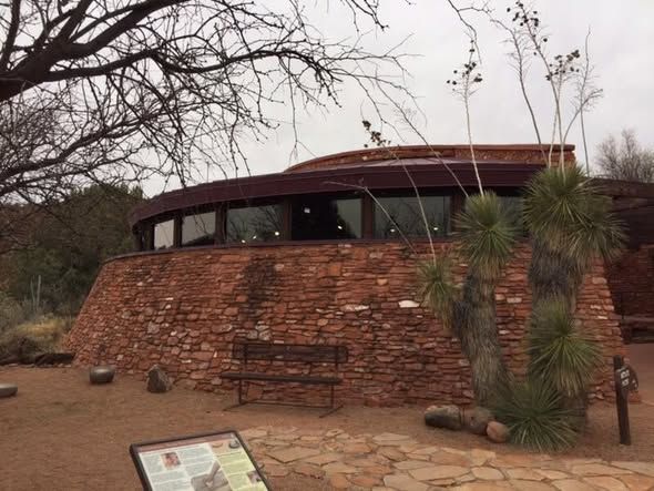 Round building made of red stone with a circular windowed upper level. A bench and plant are in the foreground.