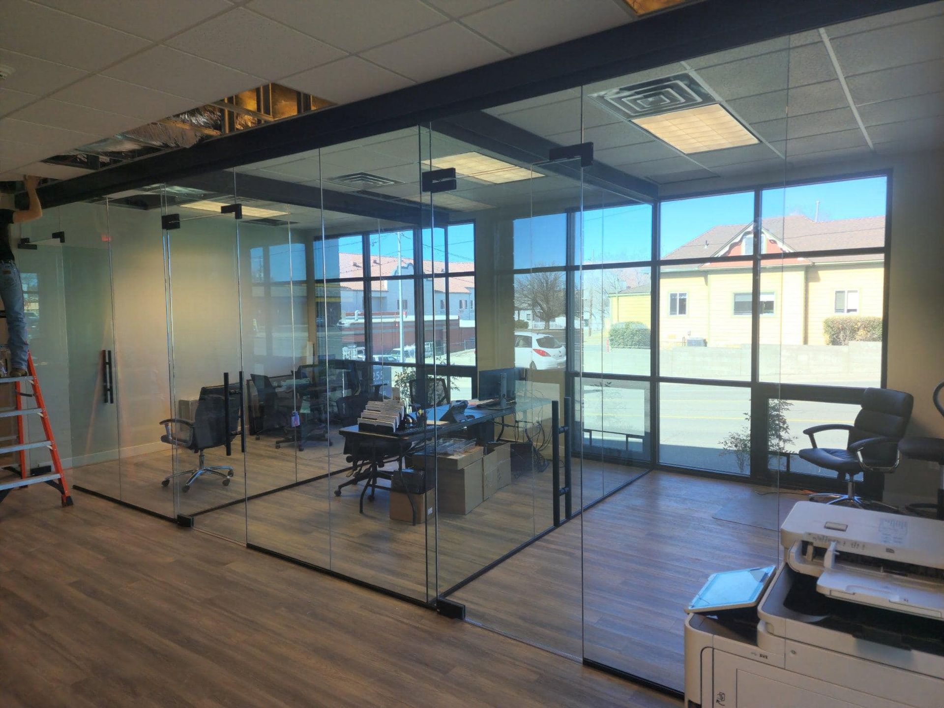 Office space with glass walls, desks, chairs, and large windows looking outside.