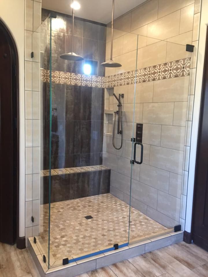 Glass-enclosed shower with tiled walls and floor. Two showerheads and a built-in bench.