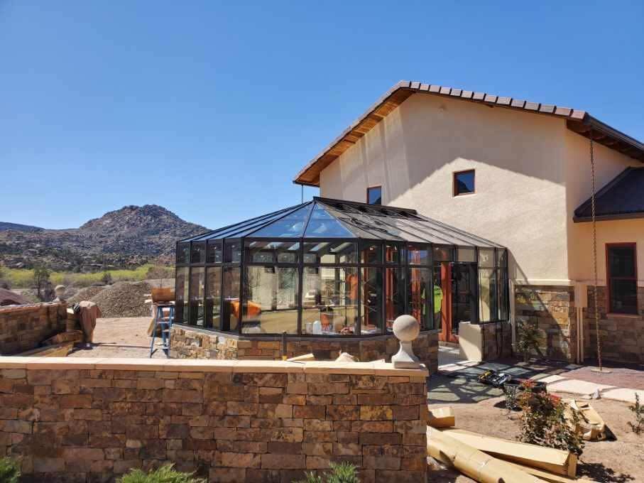 Sunroom addition to a house with a stone wall and mountain backdrop on a sunny day.