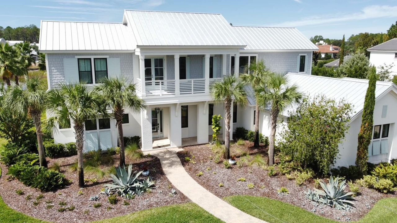 An aerial view of a large white house with palm trees in front of it.