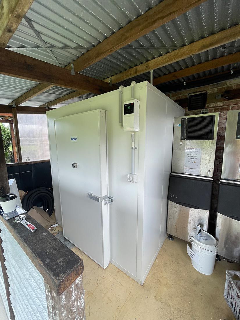 A Large White Refrigerator is Sitting in a Room Under a Roof — Condie Refrigeration & Airconditioning in Ocean Shores, NSW