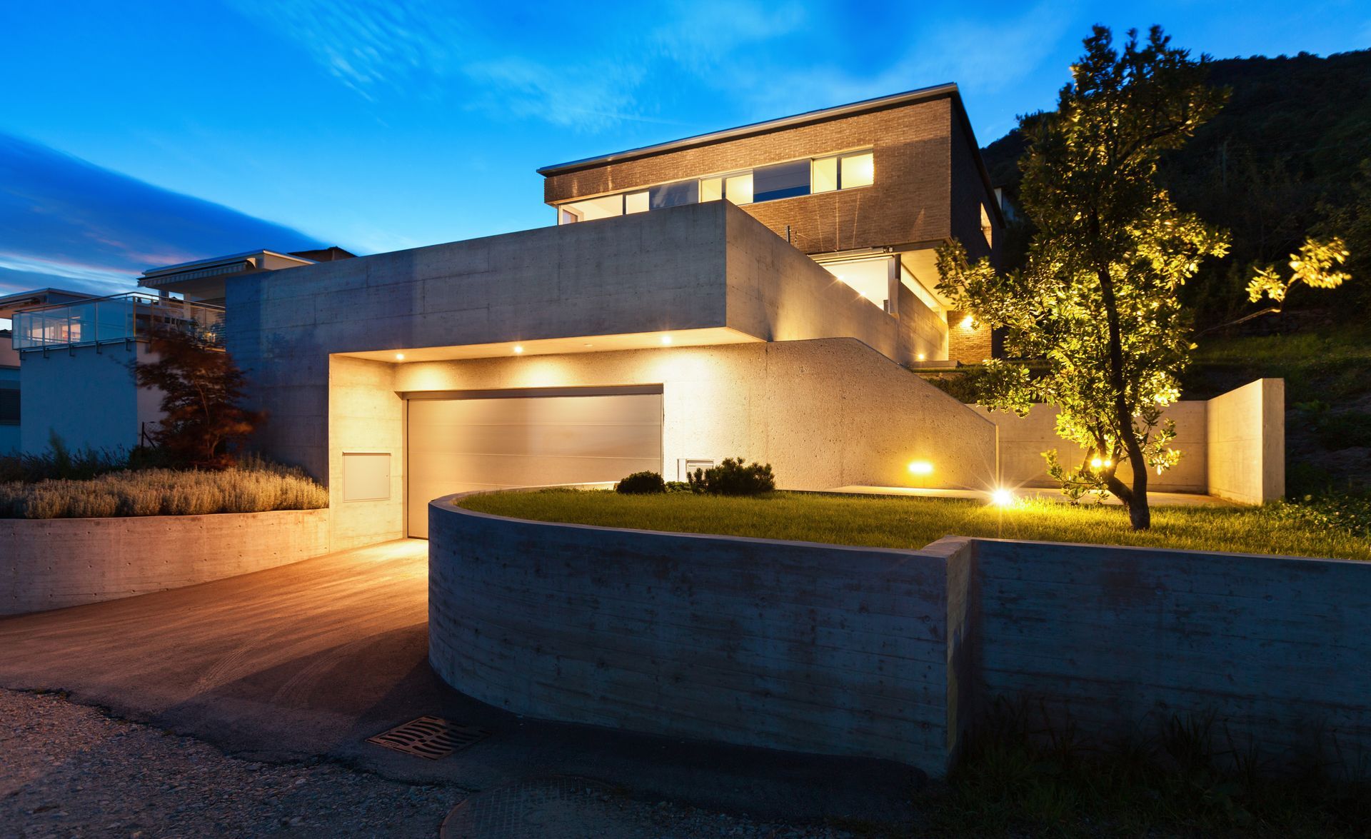 A modern house with a garage and a tree in front of it at night.