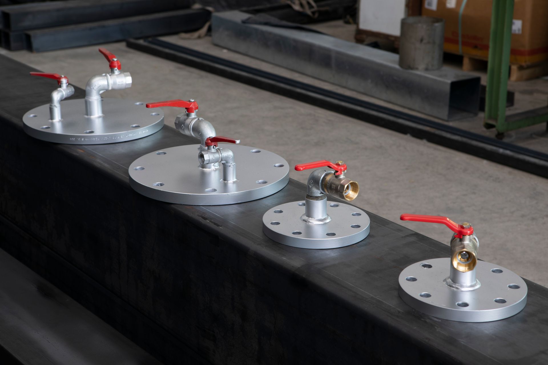 Quattro elementi metallici rotondi con valvole rosse montati in fila su una superficie industriale nera