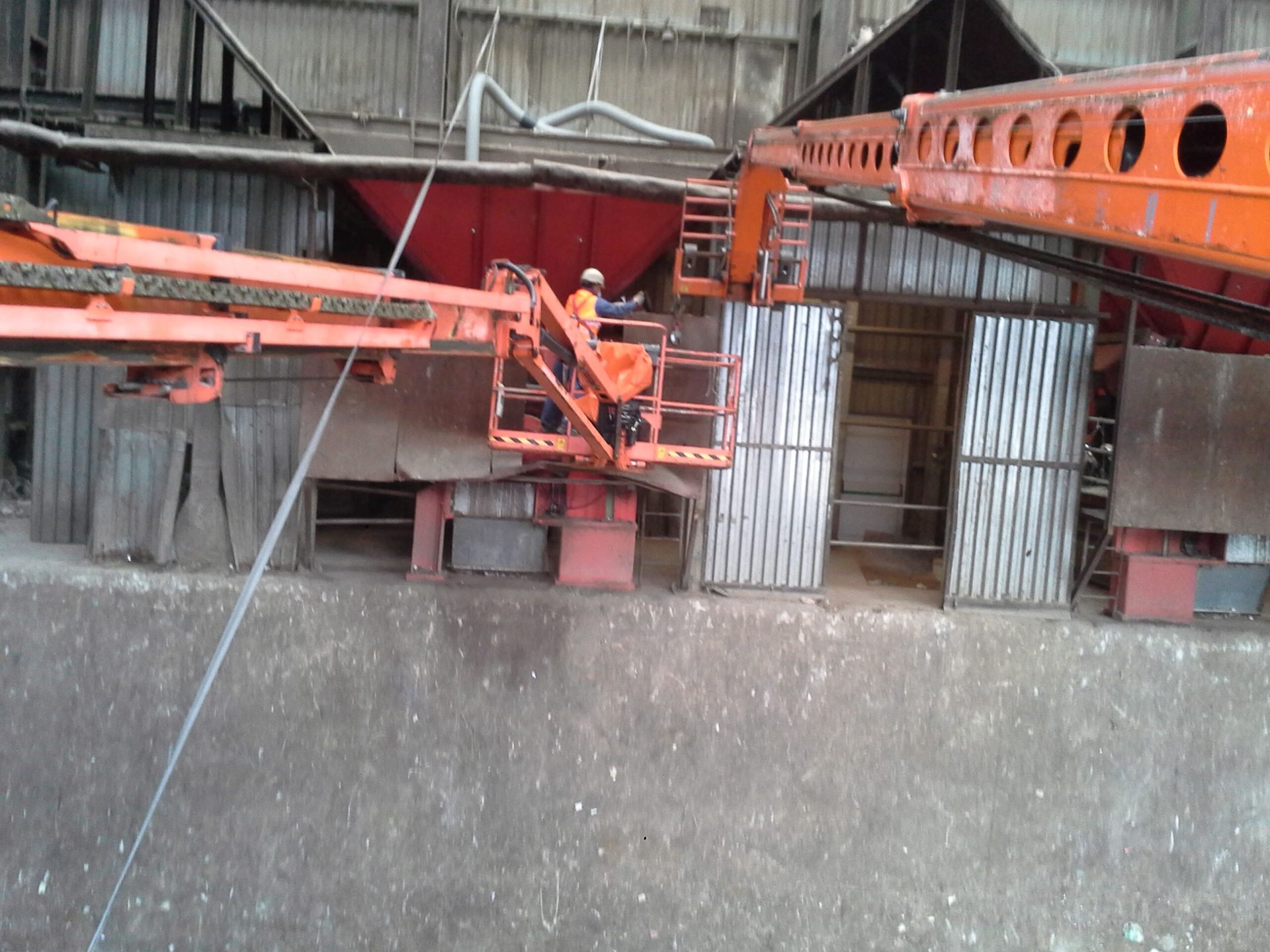 Operaio su un'impalcatura industriale arancione accanto a pannelli di lamiera ondulata in un cantiere edile.
