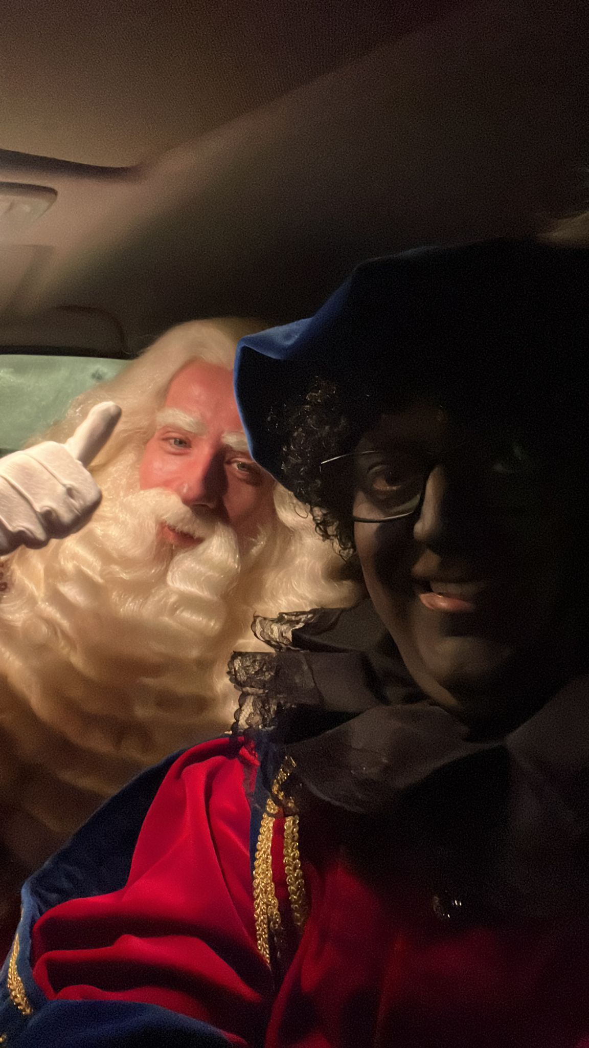 Twee verklede personen maken een selfie in een schemerig autointerieur, waarvan één verkleed is als de Kerstman.