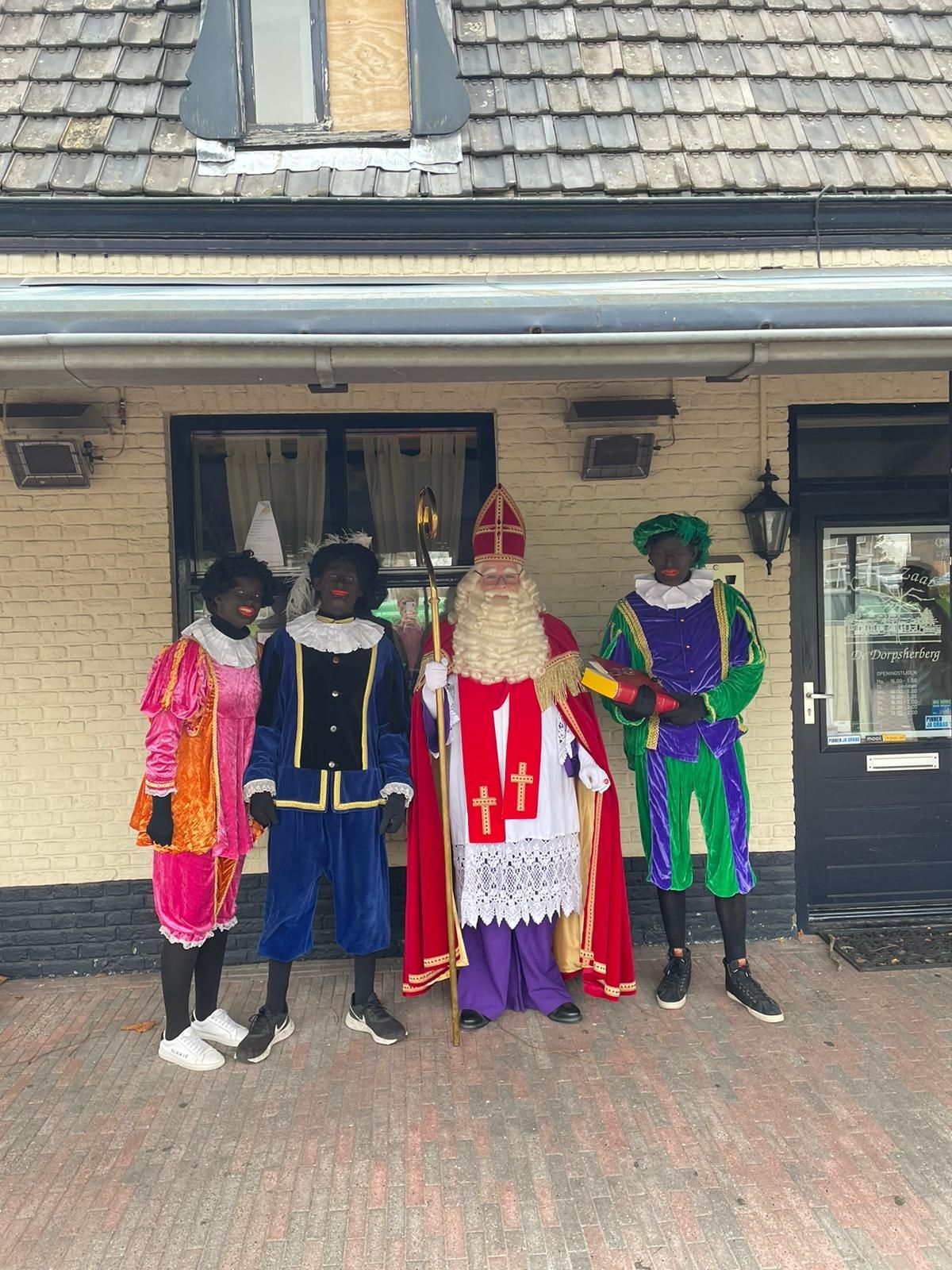 Vier mensen in kleurrijke kostuums staan ​​op een veranda voor een gebouw.