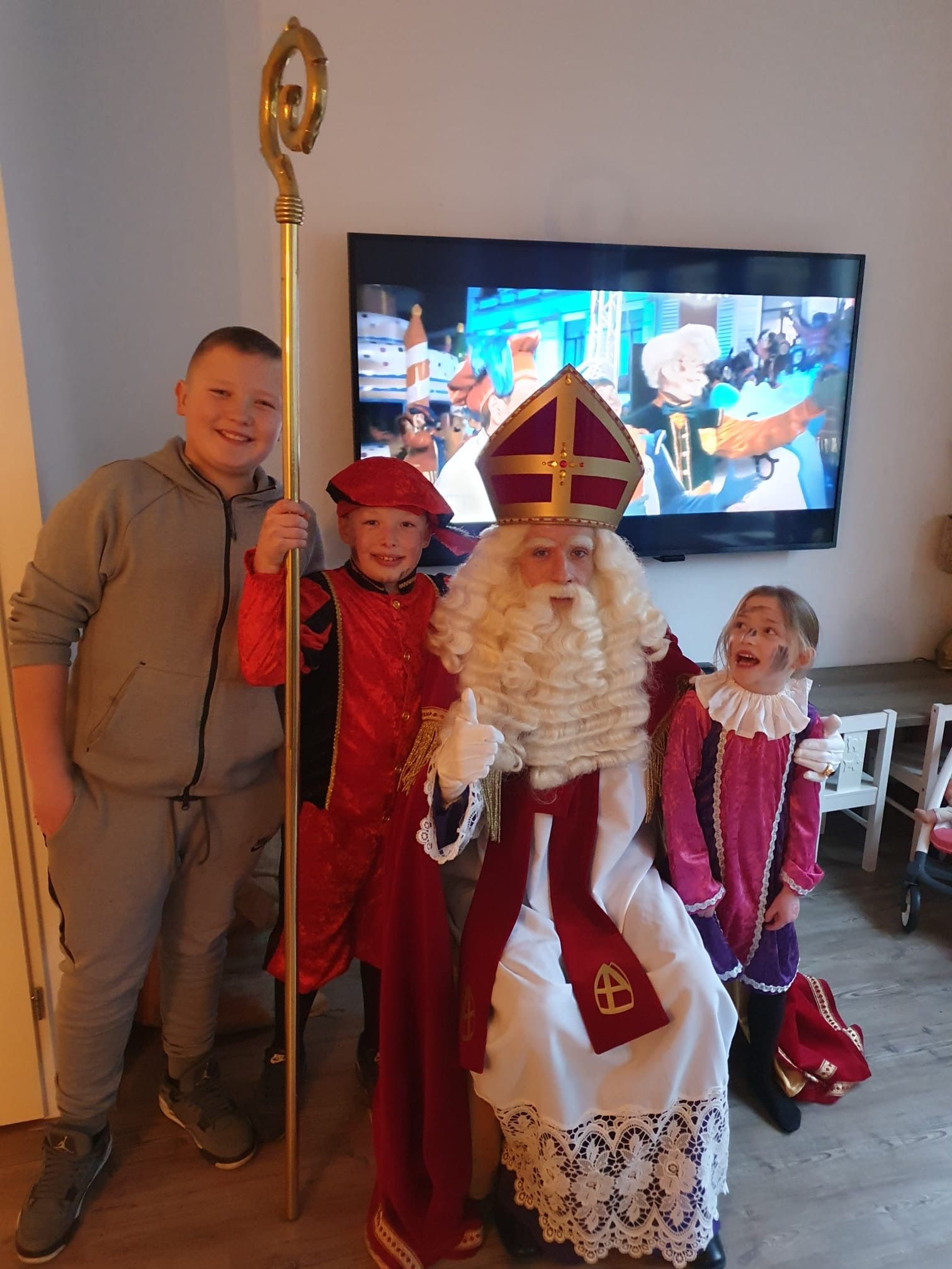 Drie volwassenen en een kind verkleed als Sinterklaas poseren binnen voor een tv.