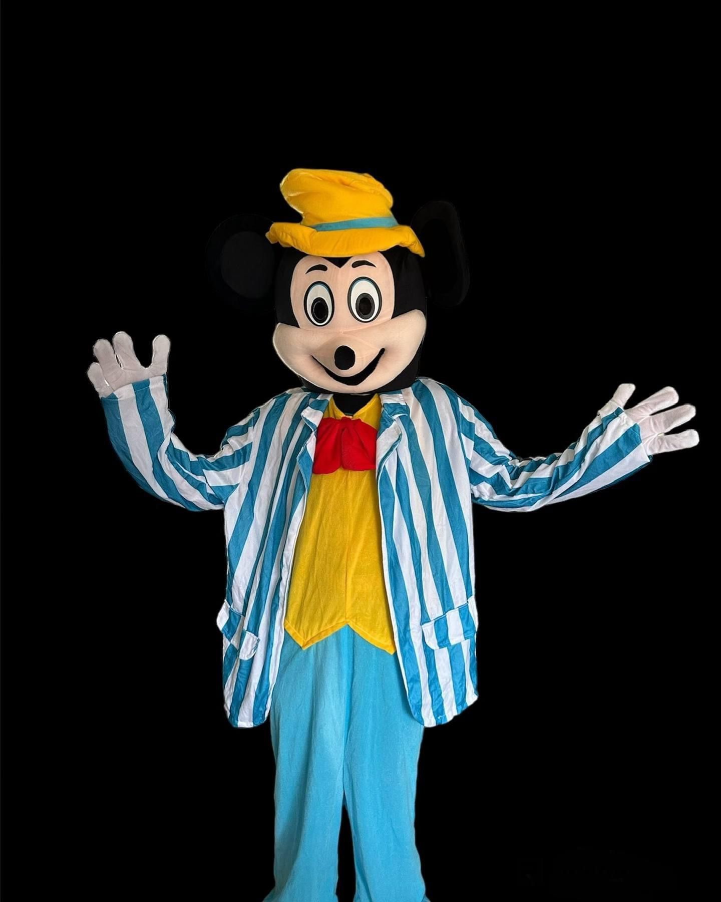 Cartoonmuismascotte in een blauwgestreepte jas, geel vest en hoed, met uitgestrekte armen op een zwarte achtergrond.