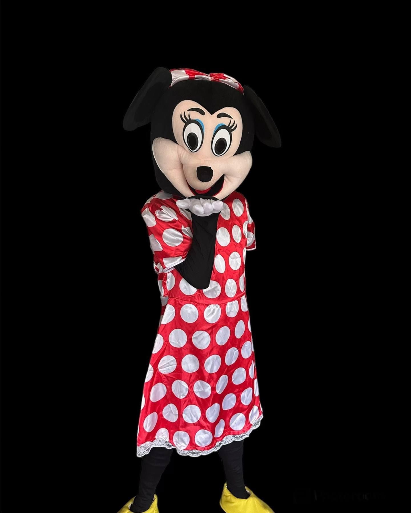 Een cartoonmuisfiguur in een rode jurk met stippen en een strik, poserend tegen een zwarte achtergrond.