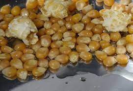 Close-up van goudgele maïskorrels op een metalen dienblad, met een paar stukjes popcorn ertussen.