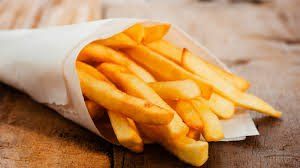 Frietjes in een wit papieren puntje op een houten tafel.