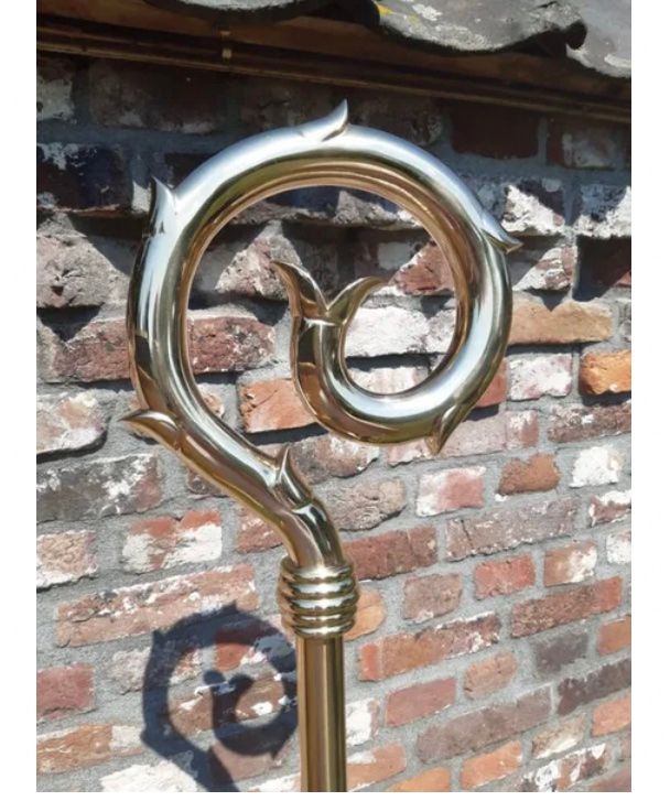 Decoratieve metalen spiraalvormige bekroning op een bakstenen muur met een schaduw eronder.