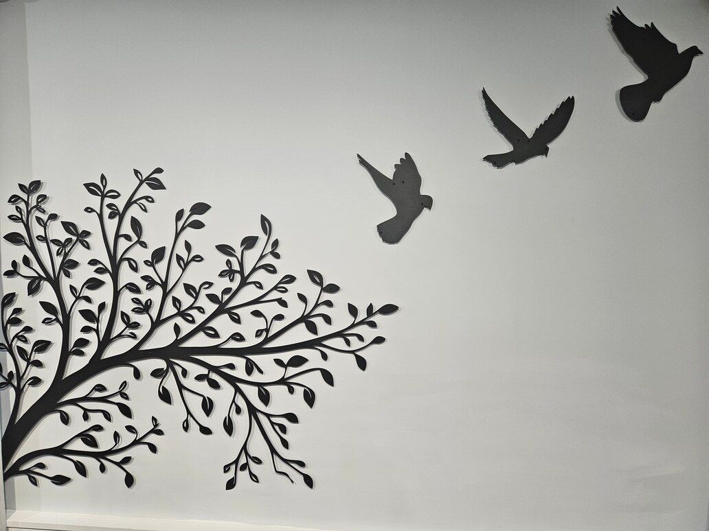 Silhouette of a tree branch with leaves and three birds flying across a light sky