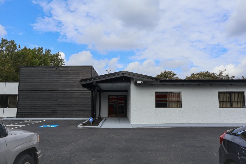 Low white and black commercial building with a central entrance and parking lot under a cloudy sky