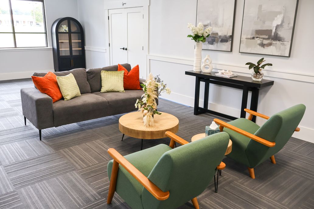 Modern living room with gray sofa, green chairs, round coffee table, and black console table