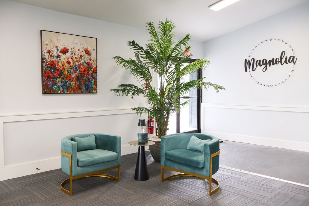 Modern waiting area with two teal chairs, a tall plant, colorful wall art, and a logo on the wall