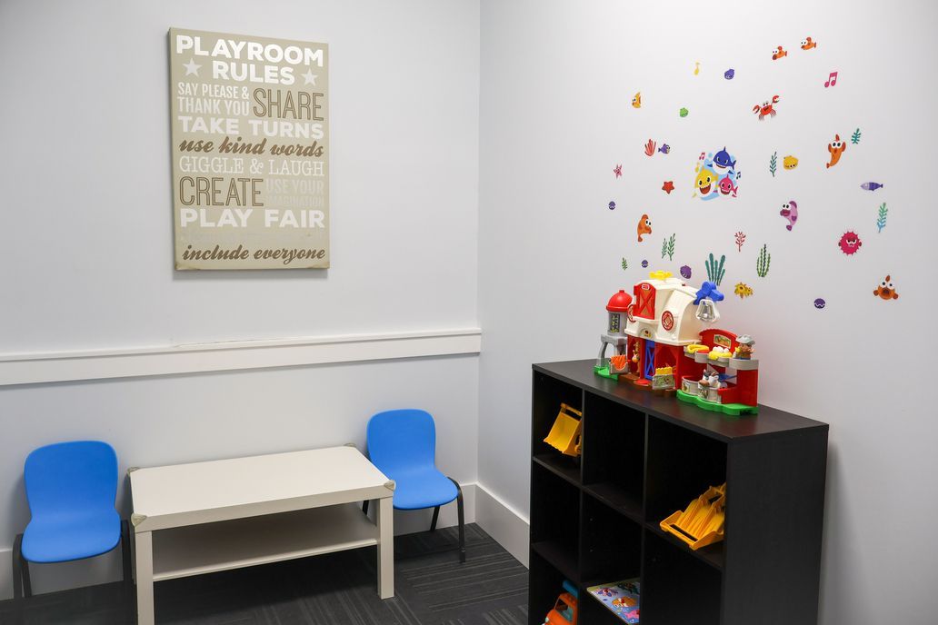 Small playroom with two blue chairs, a white table, a black shelf, and colorful wall decals.