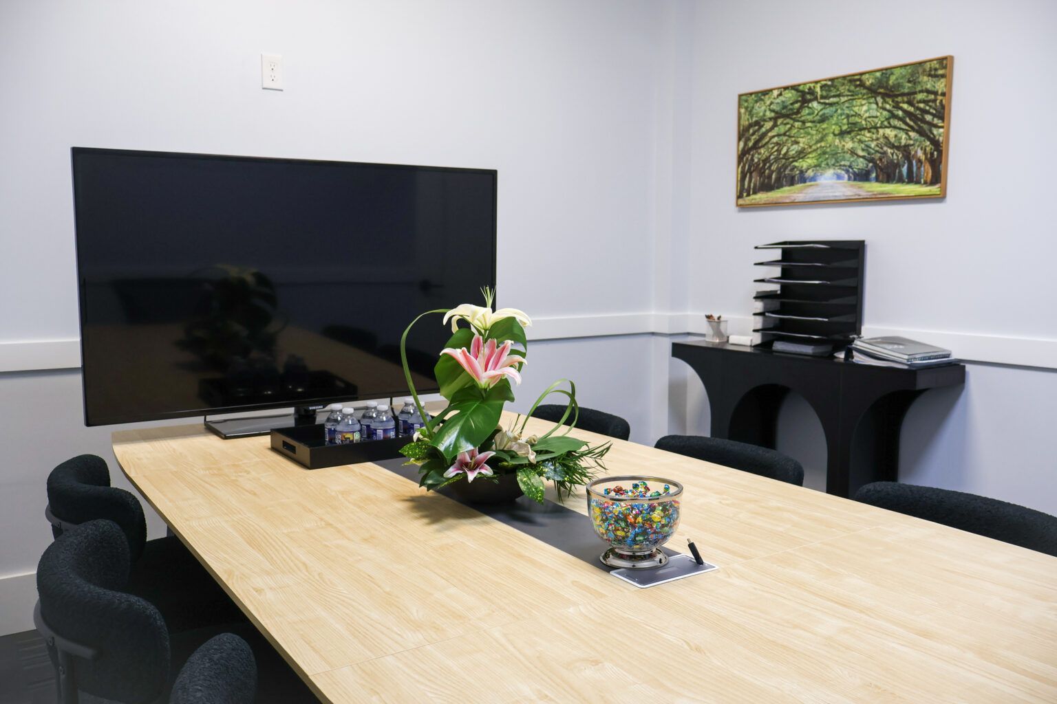 Conference room with large TV, long table, black chairs, and floral centerpiece
