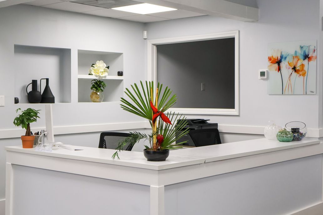 Modern reception desk in a bright office with plants, wall art, and a large blackboard-like window panel