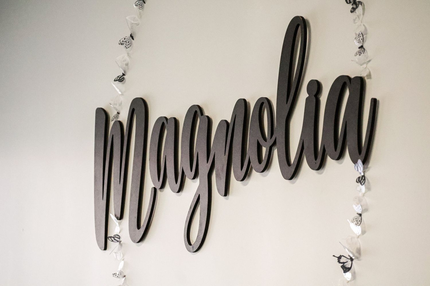 Black cursive wall sign reading magnolia with white floral garland accents