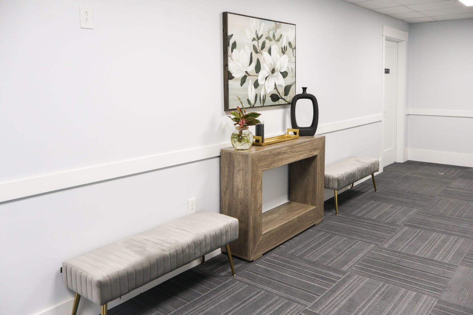 Modern hallway with benches, a console table, mirror, floral art, and patterned carpet