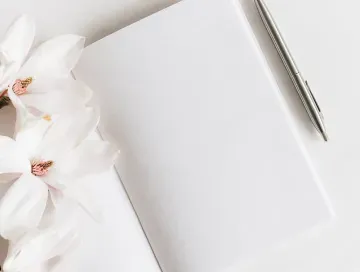 White blank paper with a silver pen beside white flowers on a light background
