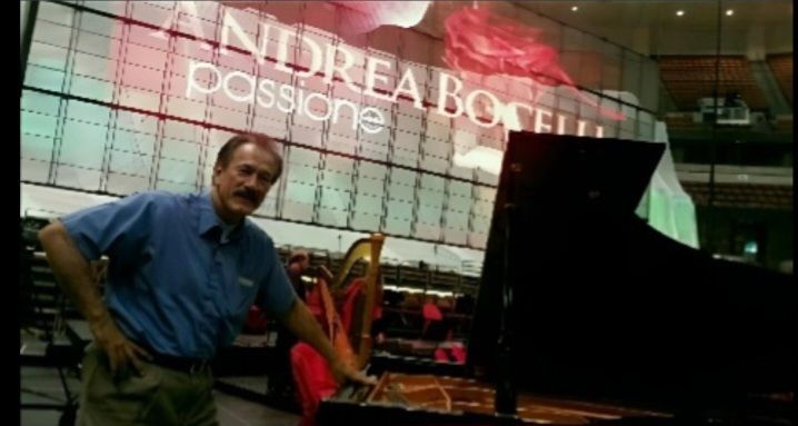 A person stands next to a grand piano in front of a stage backdrop displaying