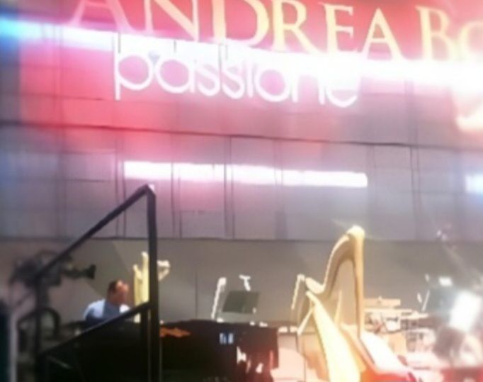 A concert stage featuring a musician at a piano, a harp, and a large illuminated backdrop reading