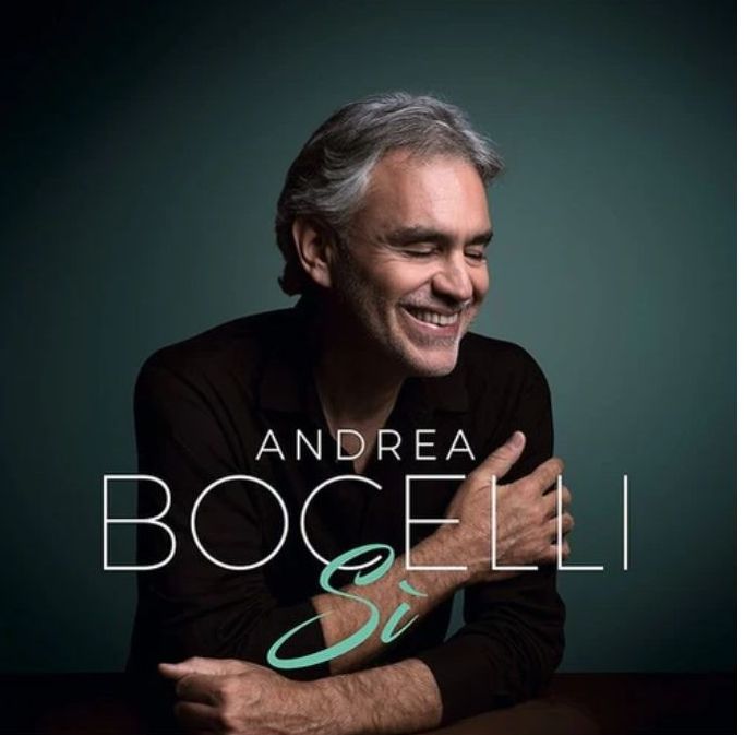 Andrea Bocelli smiling with his hand on his shoulder against a dark teal background. The album title