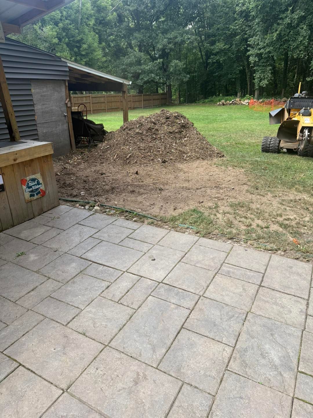 Backyard with stone patio, dirt pile, shed, and construction equipment.