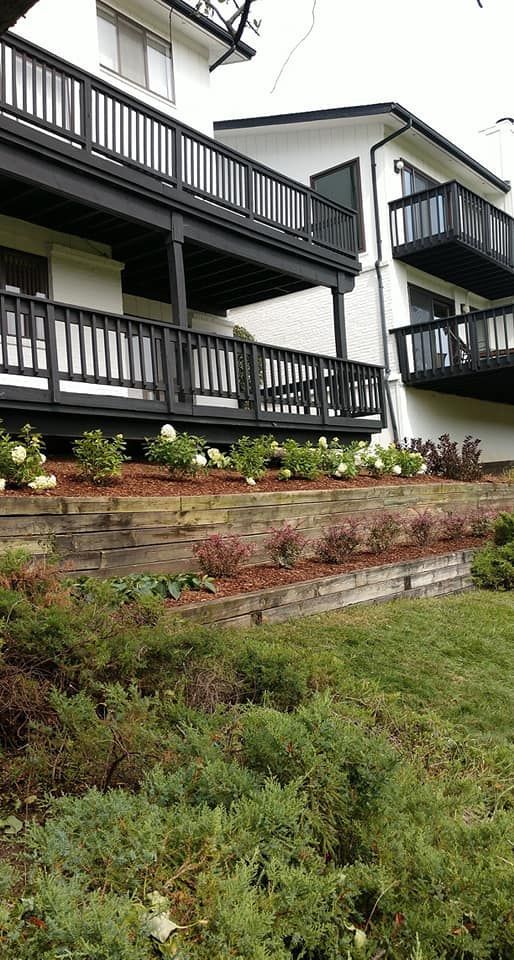 Exterior of white building with black balconies and landscaping; tiered garden with bushes and mulch.