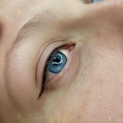 Close-up of a blue eye with black eyeliner on a light skin tone.