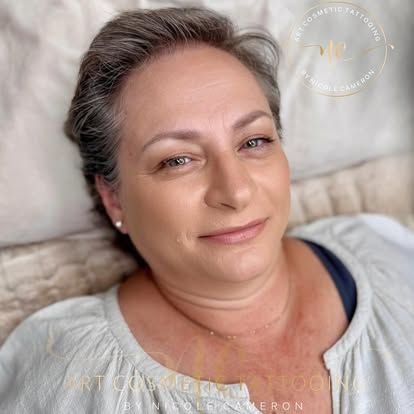 Close-up of a smiling woman reclining on a light-colored pillow, wearing a gray top.