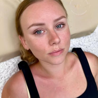 Close-up of a woman with blonde hair and blue eyes lying on a white pillow, looking at the camera