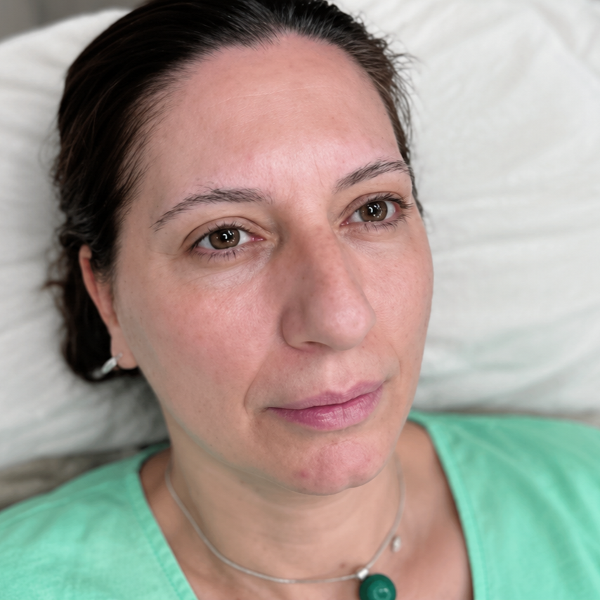 Close-up of a woman lying on a pillow in a green shirt, looking upward with a neutral expression
