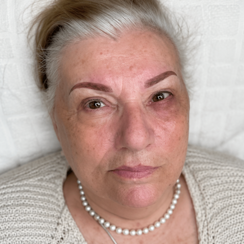 Close-up portrait of a woman with short gray hair, neutral expression, and pearl necklace on a white background