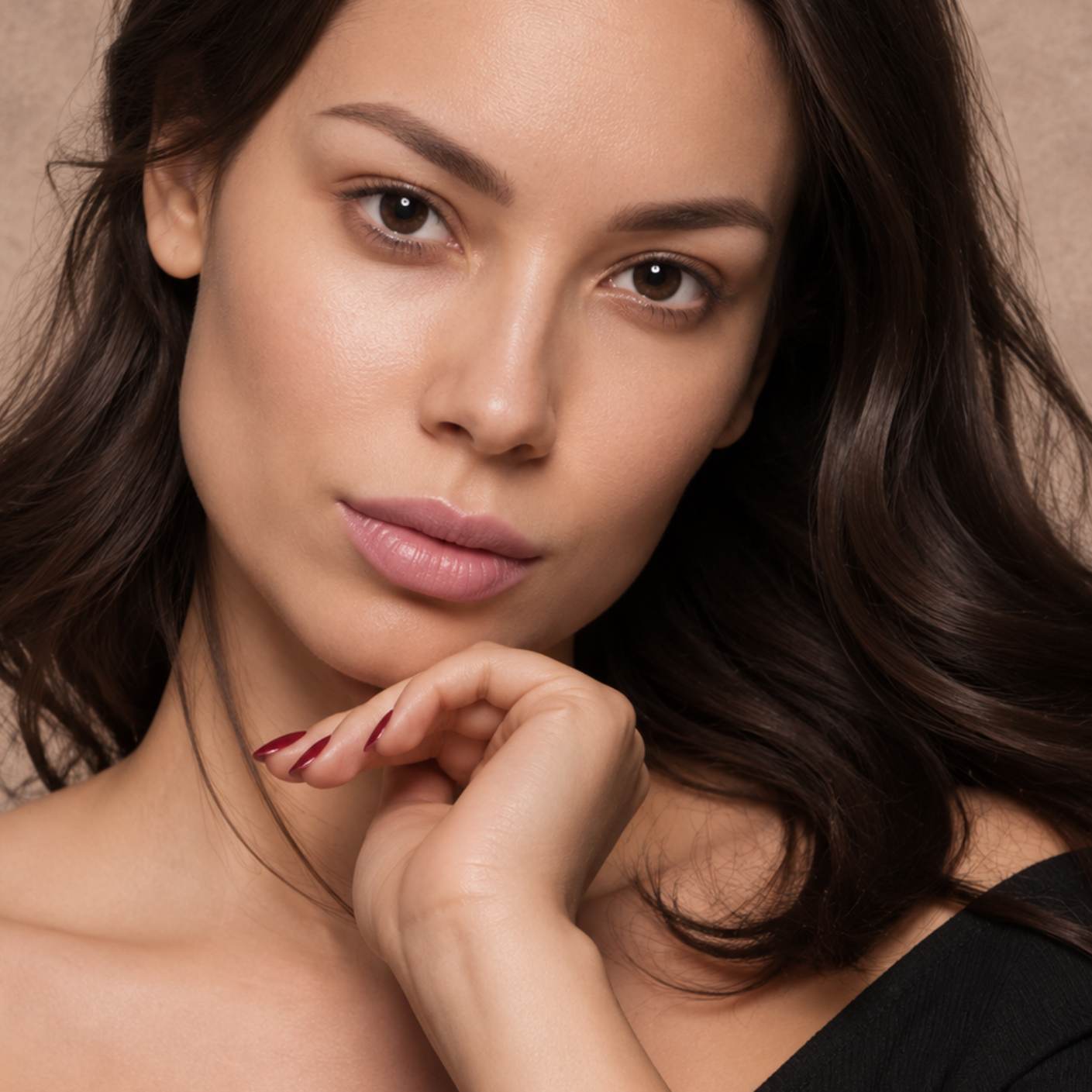 Close-up portrait of a woman with dark hair, resting her chin on her hand, looking at the camera