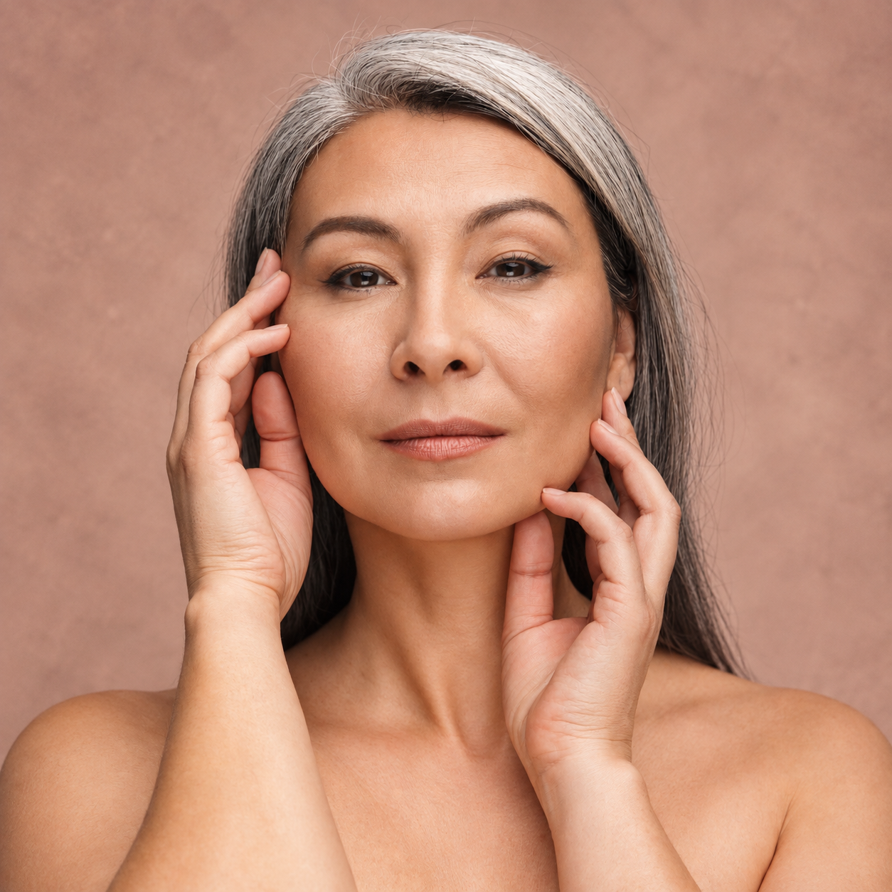 Portrait of a person with gray hair, hands framing their face against a soft peach background