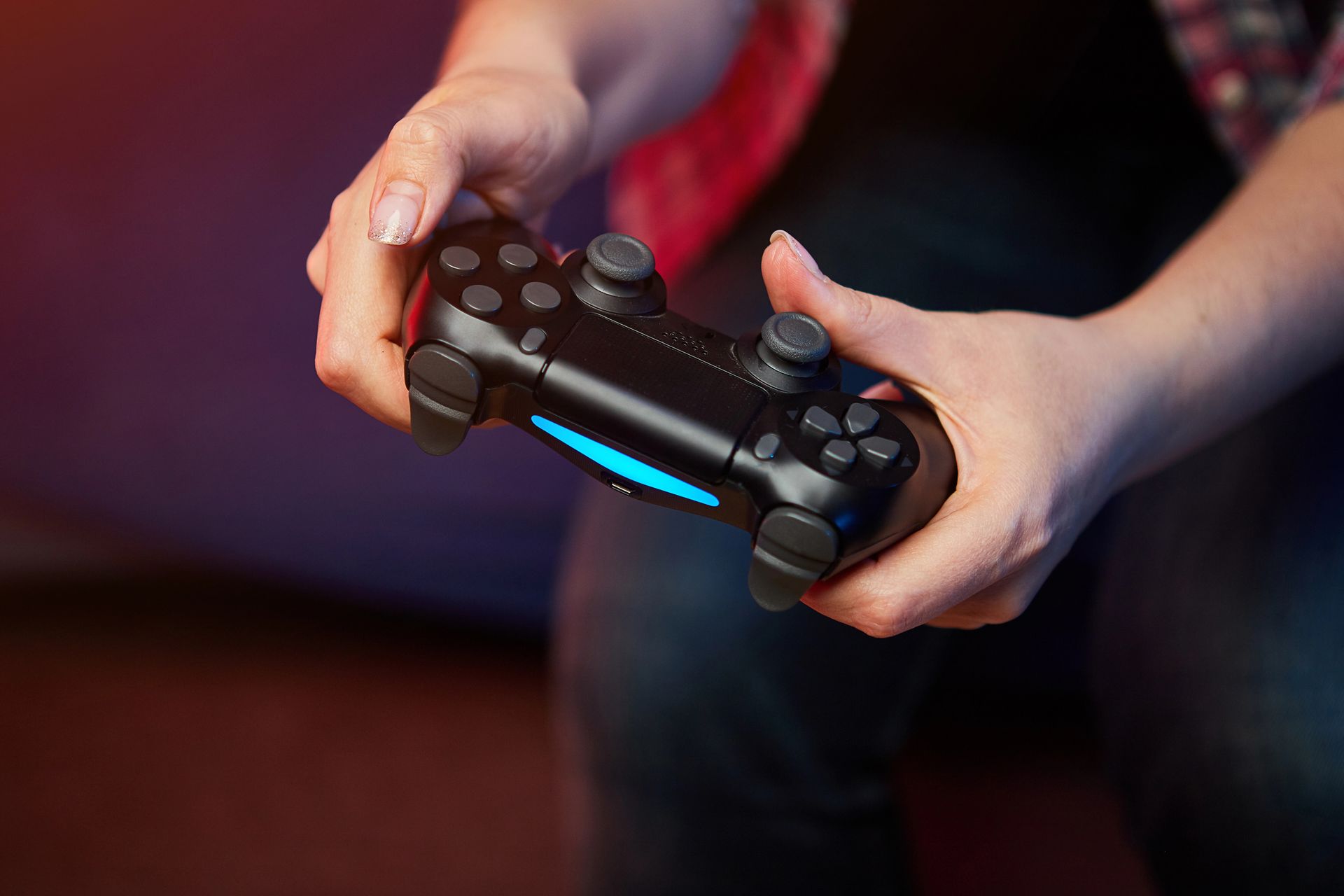 Primo piano di mani che impugnano un controller PlayStation 4 nero con una barra luminosa blu.