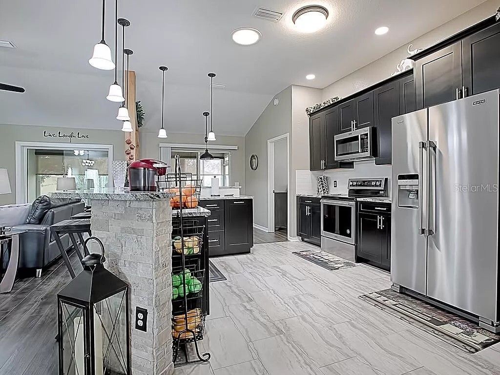 Modern kitchen with stainless steel appliances, dark cabinets, and white wooden floors.