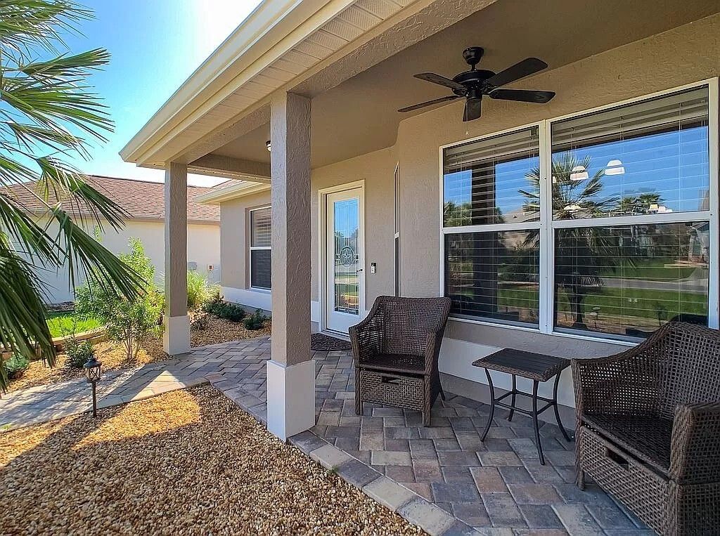 Covered patio with wicker furniture, brick floor, beige walls, and a ceiling fan.