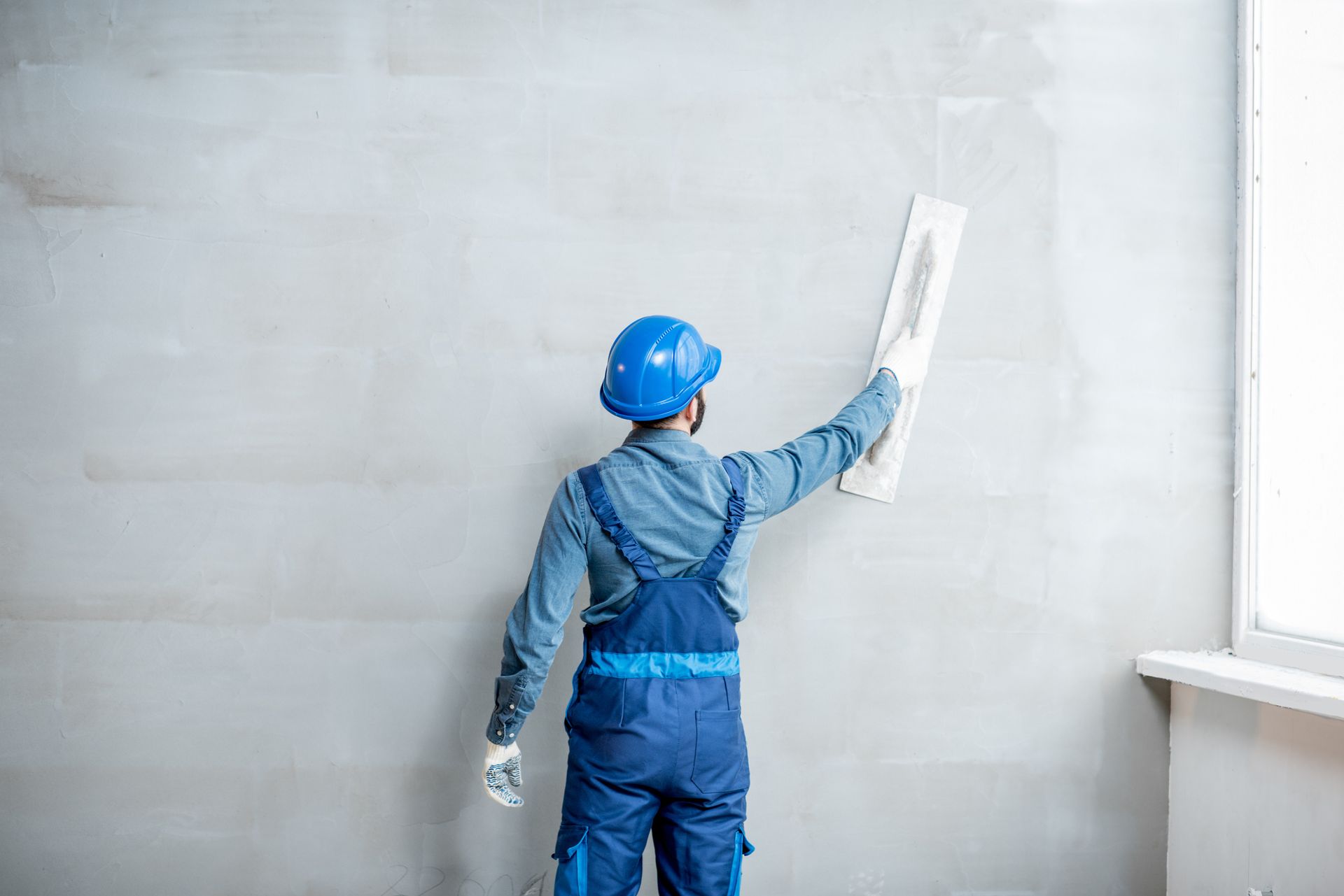 A man is plastering a wall with a trowel.